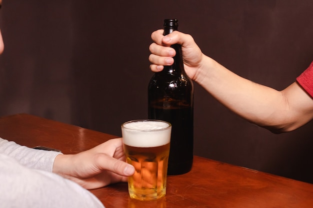 Neem detail van een man die een glas bier vasthoudt, terwijl de barman de fles vasthoudt.