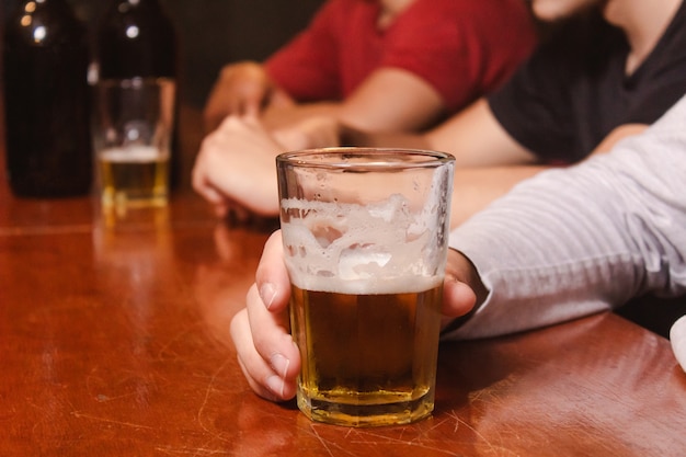 Neem detail van een man met een glas bier aan de bar.