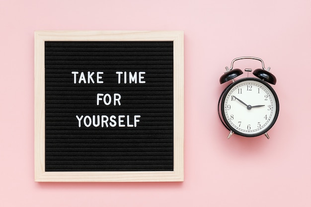 Neem tijd voor jezelf. Motiverende citaat op letterbord en zwarte wekker op roze