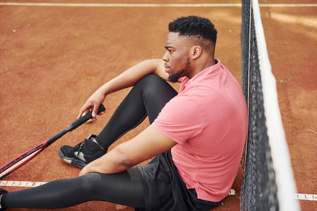 Neemt een pauze Afro-Amerikaanse man in roze shirt speelt tennis buiten op de baan