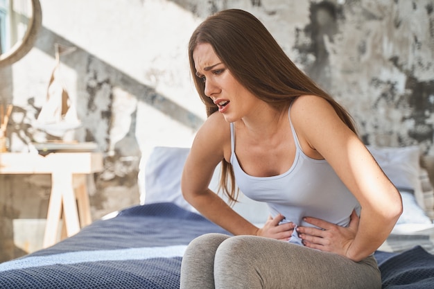 Negative delighted brunette woman making face and touching her stomach while suffering pain