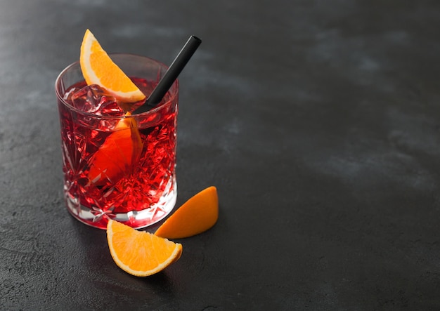 Negroni cocktail in crystal glass with orange slice and black straw on black table background Top view