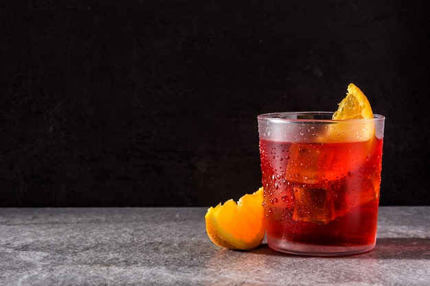 Negroni cocktail with piece of orange in glass on black, copyspace