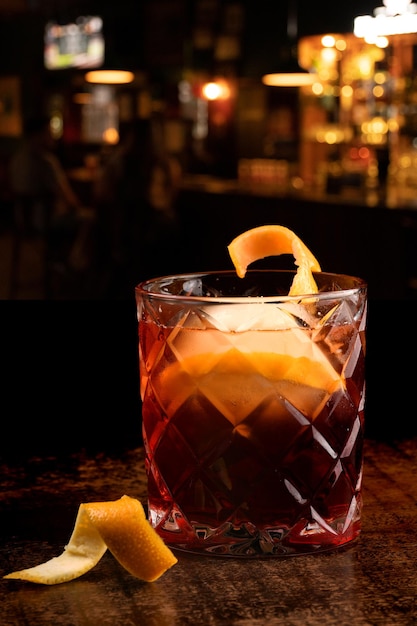 Negroni cocktail with round ice on wooden table top view with blurred pub background