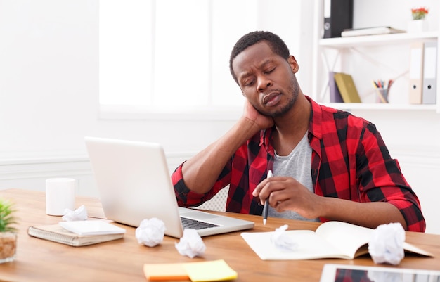 Nek pijn. gestresste afro-amerikaanse werknemer die met laptop op kantoor werkt. overstuur tijdens het werken aan een nieuw project, kopieer ruimte