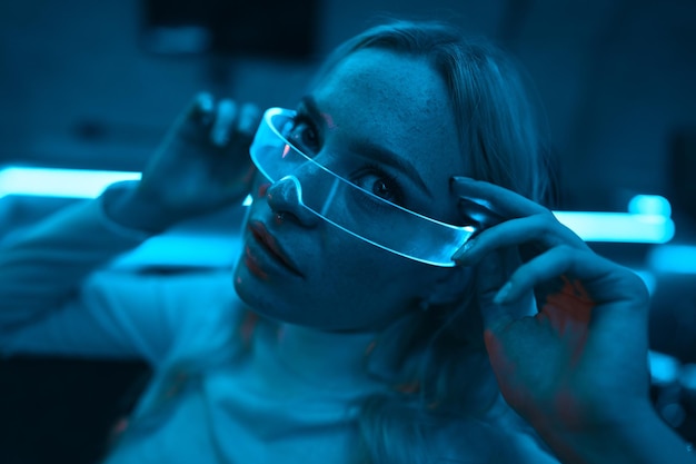 Neon blue light falls on a young woman wearing futuristic glass glasses