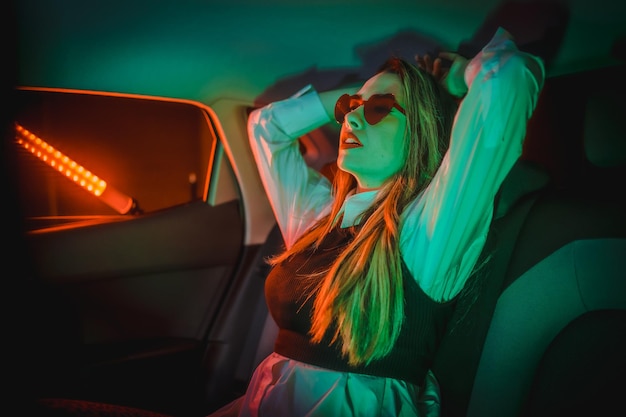 Neon photography inside a car of a young blonde woman with heart glasses