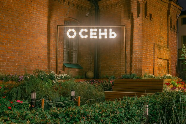 Неоновая вывеска в парке с надписью Осень на русском языке, на фоне красивой кирпичной стены