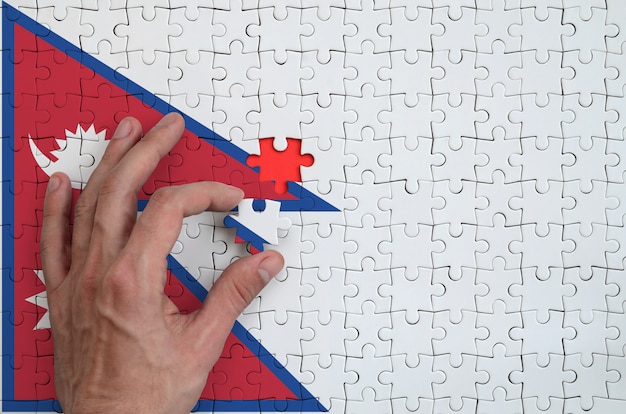 Nepal flag  is depicted on a puzzle, which the man's hand completes to fold