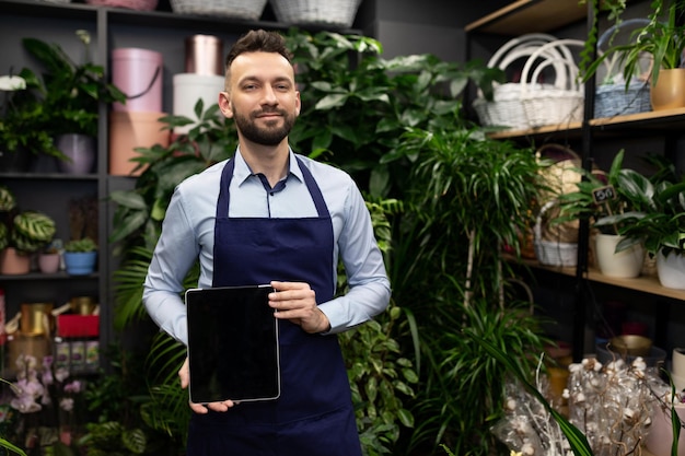 Nerd at flower shop demonstrating tablet screen next to shelves with potted plants