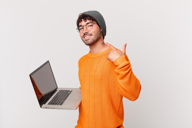 Nerd man with computer smiling confidently pointing to own broad smile, positive, relaxed, satisfied attitude