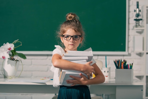 Nerd school girl in glasses with books on blackboard kid girl learning lesson at school elementary s