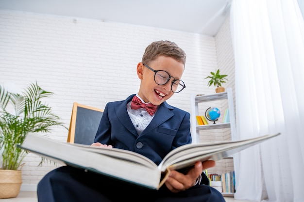 Nerd schoolboy with glasses looks at book and smiles.