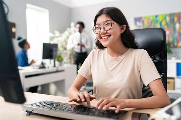 Nerd woman in big glasses with smile sits in comfortable chair in front of desk