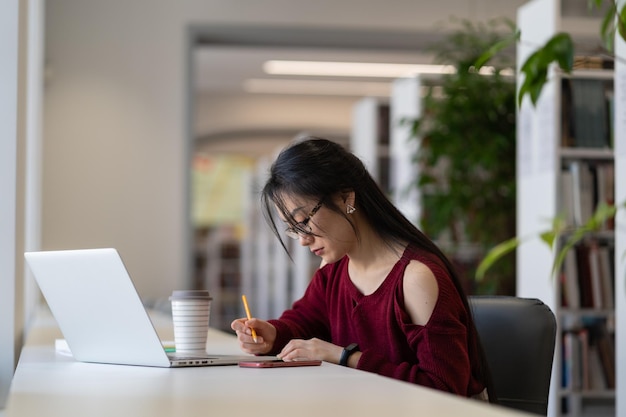 Nerdy Aziatisch meisje met een bril die werkt aan een universitair onderzoeksproject in de bibliotheek