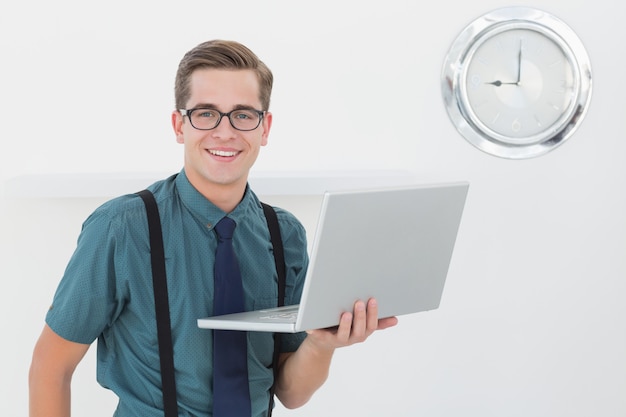 Nerdy businessman holding laptop smiling at camera