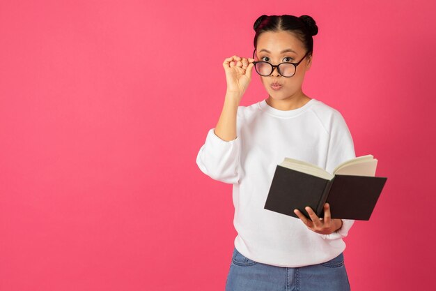 Nerdy young asian woman holding book and adjusting glasses