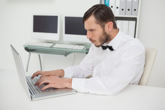 Nerdyzakenman die aan laptop bij bureau werkt