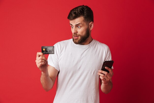 Nerveus jonge man met mobiele telefoon en creditcard.