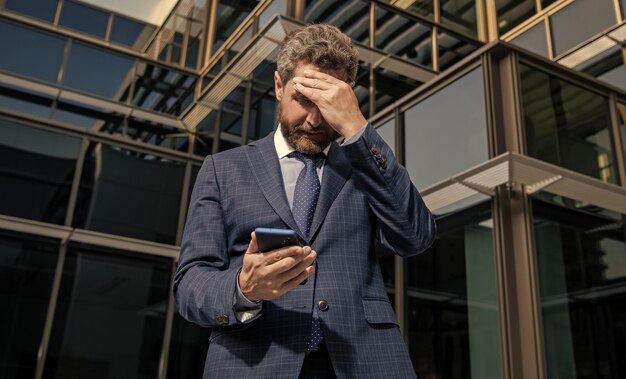 Nerveuze ondernemer in zakelijk pak kijkend naar telefoon buiten kantoor angst