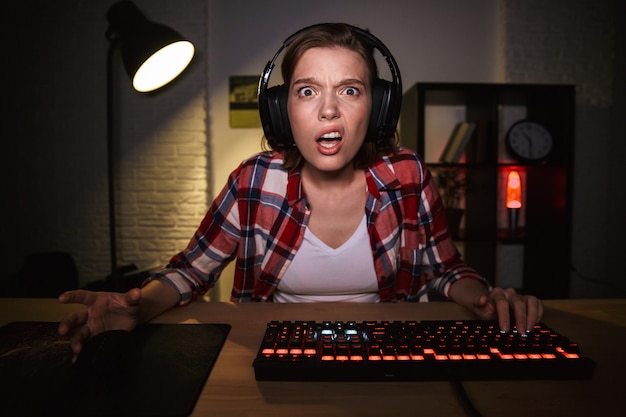 テーブルでオンラインコンピュータゲームをプレイする神経質な怒っている若い女性ゲーマー