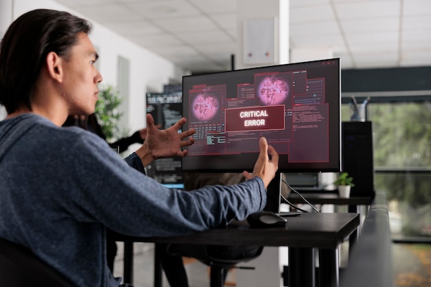 Nervous app developer having system error message on computer screen, trying to solve hacking alert problem. System engineer looking at hacked server on pc monitor in it office room.