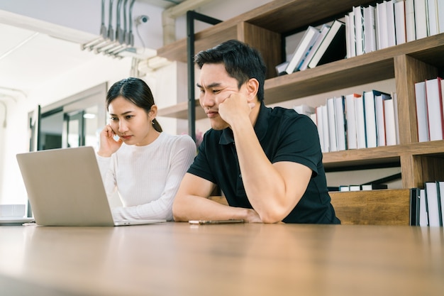 The nervous Asian male and female sitting in front of a laptop, looking with a bad and uncomfortable feeling.