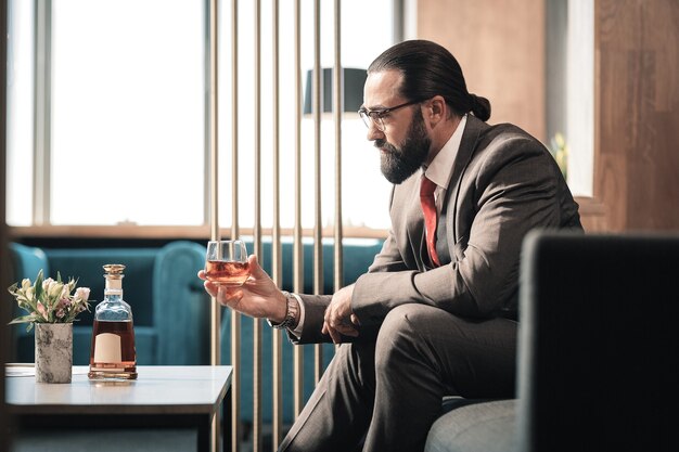 Nervous breakdown. Bearded mature businessman suffering from nervous breakdown drinking alcohol