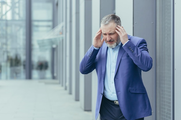 Nervous breakdown exhaustion senior man businessman stands on\
the street near the office center and