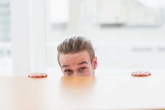 Nervous businessman peeking over desk