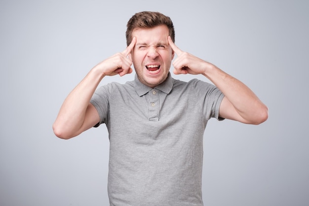 Nervous caucasian guy pressing his temples with fingers