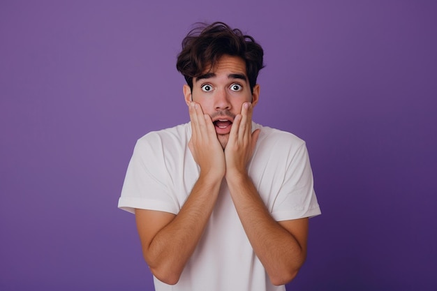 Nervous Latin man and biting nails in studio with oops reaction on purple background