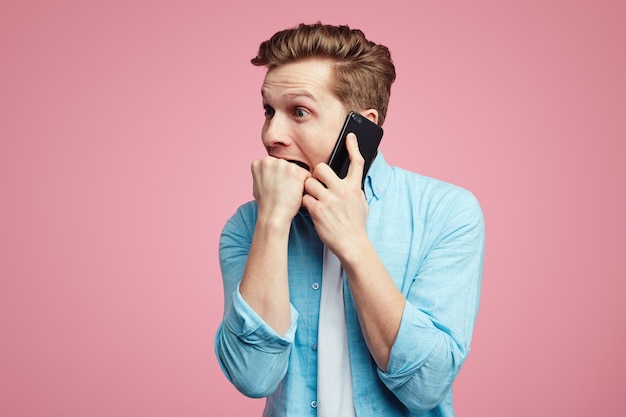 Nervous male keeps fists in mouth during conversation via smartphone