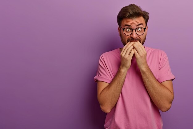 Nervous man and biting nails in studio with oops reaction to gossip on purple background Mistake sorry fake news drama or secret with regret shame or awkward