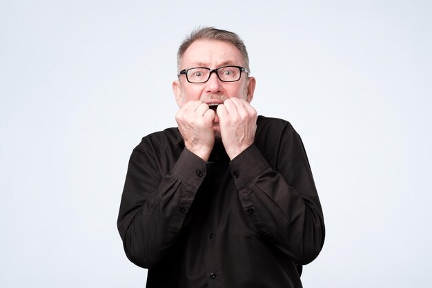 Nervous senior man in glasses bites nails looks worried before visiting doctor