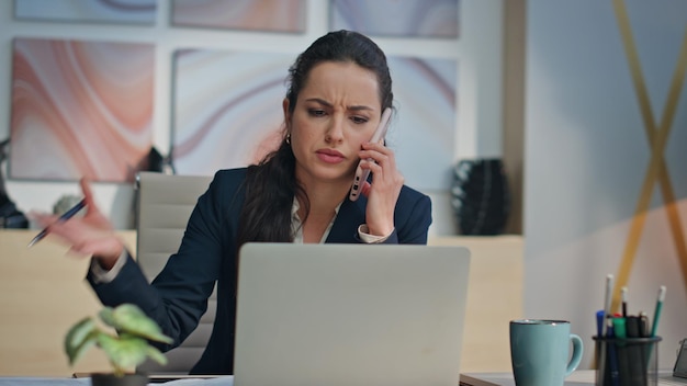Nervous woman talking cellphone looking papers in office angry manager calling