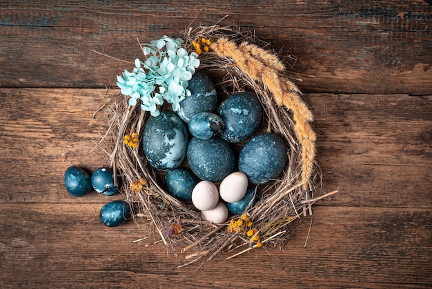 Гнездо украшено голубыми цветами с пасхальными мраморно-синими яйцами на деревянном фоне.