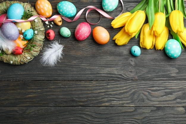 Nest met kleurrijke paaseieren, bloemen en veren op houten achtergrond