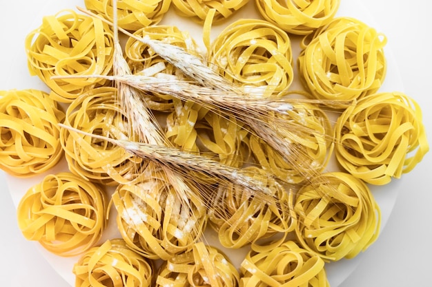 Nido di pasta di grano duro cosparso di farina su uno sfondo bianco closeup spighette di grano cucina casalinga pasta sfondo