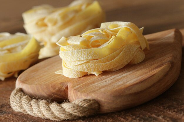 Nest of pasta tagliatelle on wooden cutting board aon rustic background Selective focus