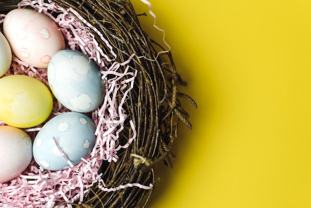 A nest of twigs and hay and a pink paper filler with pastel colored Easter eggs. Colored eggs for the holiday of light Easter background