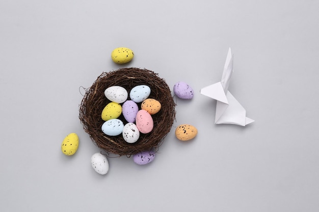 Nest with colored quail eggs and origami easter bunny on gray background Easter composition