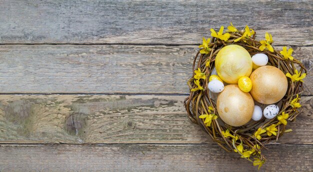 Nest with golden and yellow eggs with flowers on wooden texture Copy space for your Easter text