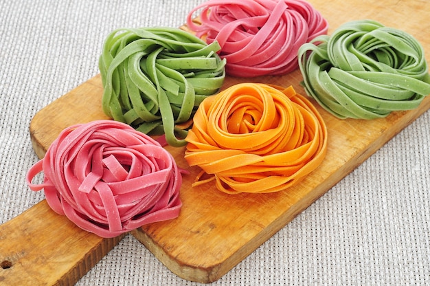 Nests of colorful pasta tagliatelle on wooden cutting board