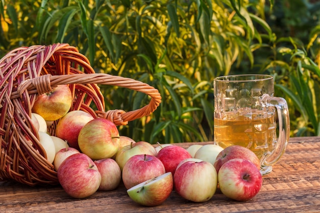 Net appels geplukt in een rieten mand en appelcider in glazen beker op houten planken