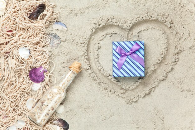 Net, shells with bottle and gift box on sand.