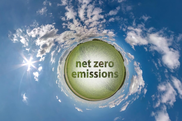 Photo net zero emissions text concept image against green tiny planet in blue sky with beautiful clouds