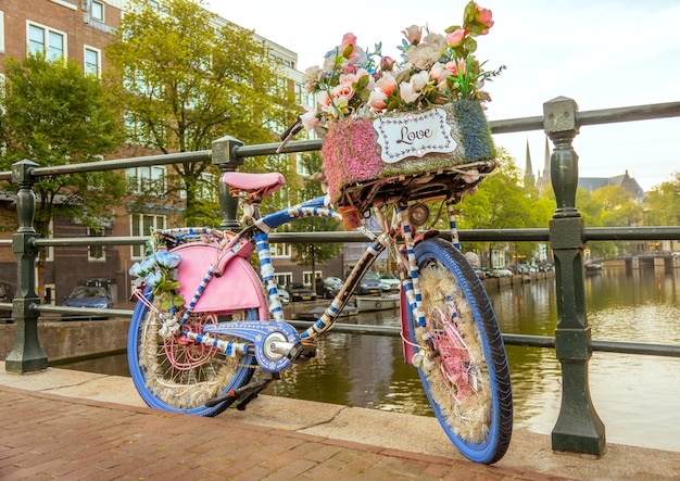 Netherlands. Cloudy morning on the Amsterdam canal. A flower-decorated bicycle with a LOVE sign is parked by the bridge fence