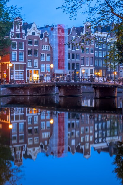 Olanda. la mattina presto ad amsterdam. ponte con biciclette parcheggiate e riflessi di case tradizionali nell'acqua del canale