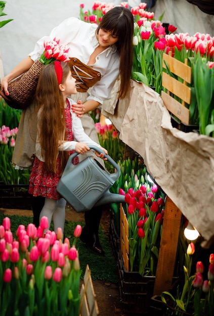 Netherlands March 23 2023 A little girl and her mother water flowers in the home garden with a watering can Children's clothing